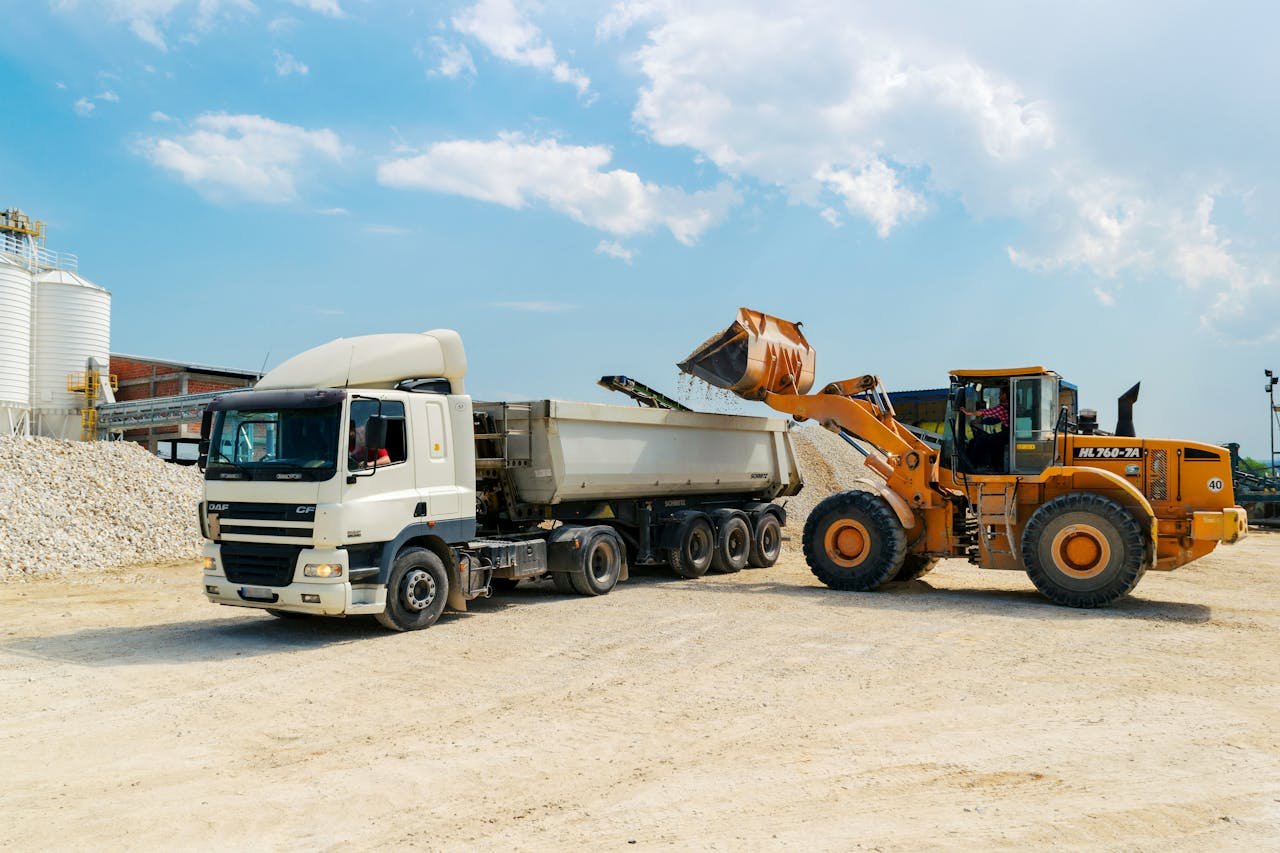 Excavator loading materials into a heavy-duty truck at a sunny construction site.