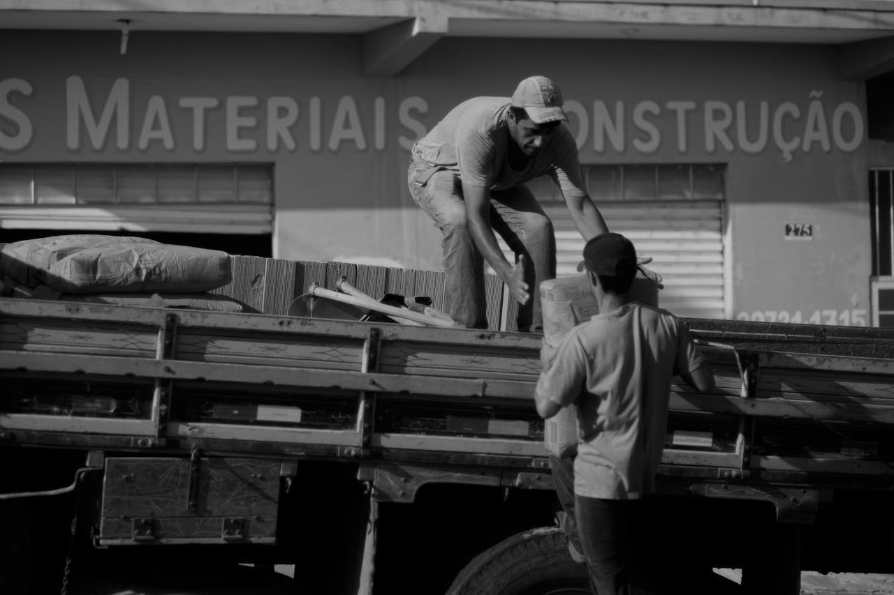 Two men load construction materials onto a truck outside a store.